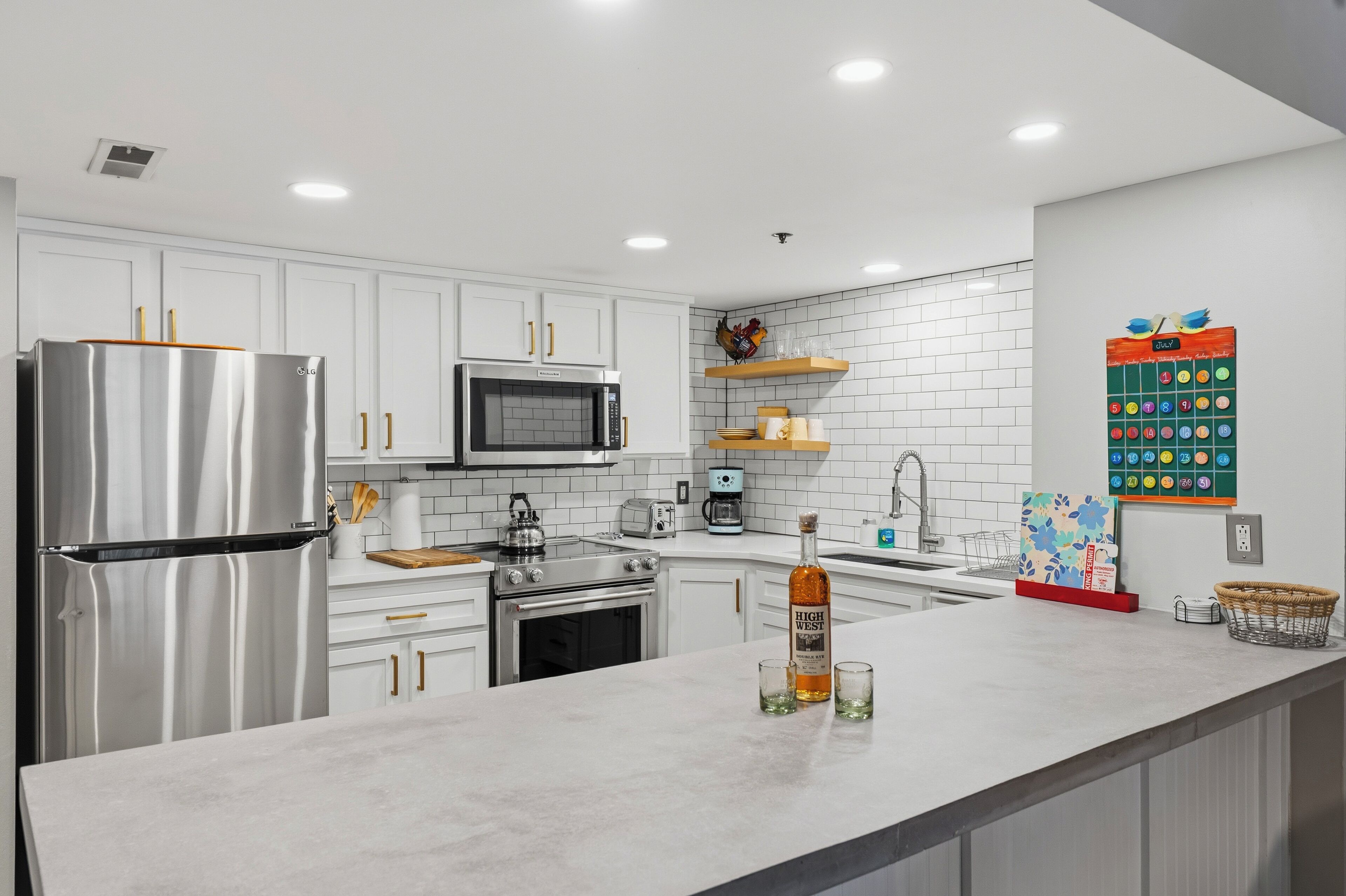 A modern kitchen with stainless steel appliances, white cabinetry, and a calendar on the wall.