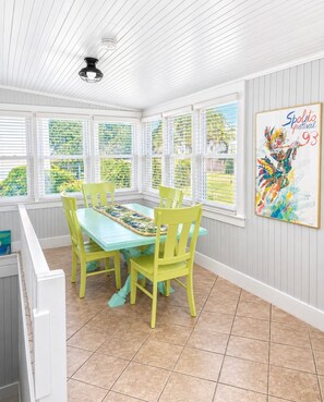 A dining area with a light blue table and yellow chairs, white paneled walls, and a window with a view of greenery. - Across the street from  beach with ocean views and access/close to restaurants! (Isle of Palms)
