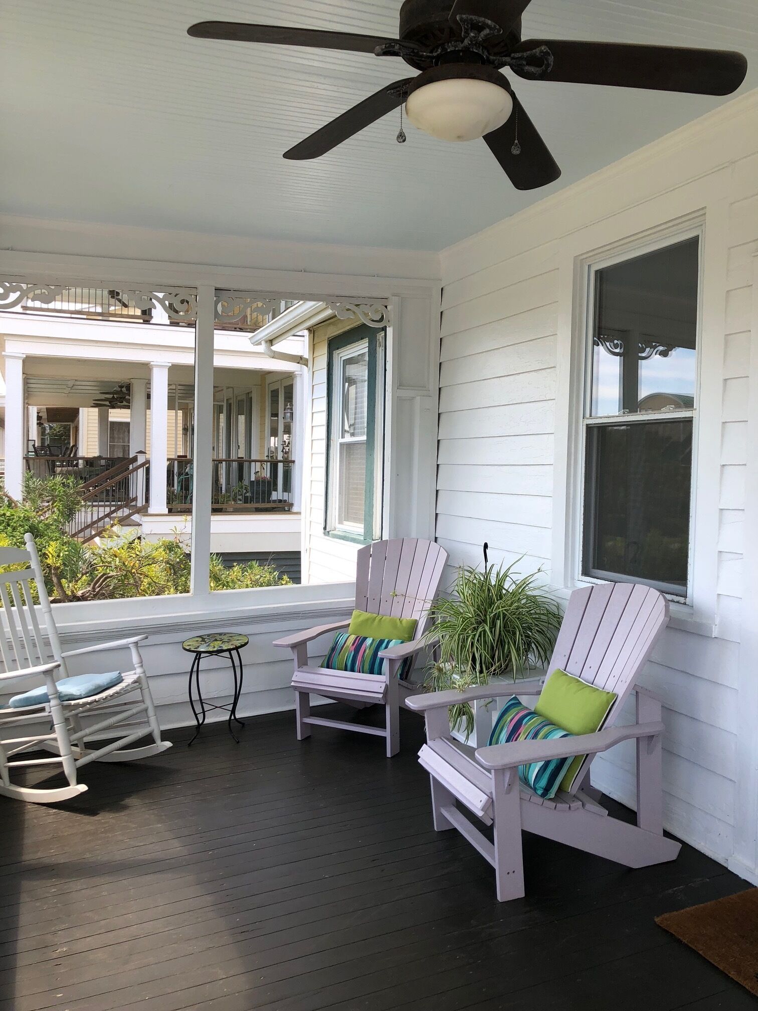 A porch with two rocking chairs and a table, a ceiling fan, and a view of a house.