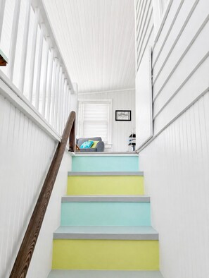 A staircase with white railings and a wooden handrail, leading to a room with a window and a framed picture on the wall. - Across the street from  beach with ocean views and access/close to restaurants! (Isle of Palms)