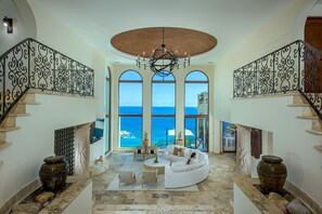 A spacious living area with a white sofa, coffee table, and decorative vases, overlooking the ocean through large windows. - Casa Rio de Luna: 7BR Ocean-View Villa with Pool, Rancho Cerro Colorado (Los Cabos)