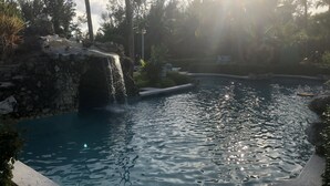 Una piscina con una cascada, rodeada de palmeras y un muro de piedra.