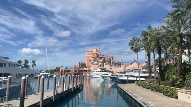 Un puerto deportivo con yates amarrados, cielo despejado y un gran edificio de resort al fondo.