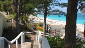 Una escalera de madera que conduce a una zona de playa con un letrero colorido, rodeada de árboles y una vista despejada del mar.
