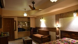 A cozy bedroom with a bed, a chair, a small table, a ceiling fan, and a mirror. - Prem Niwas Boutique Hotel (Jaipur)