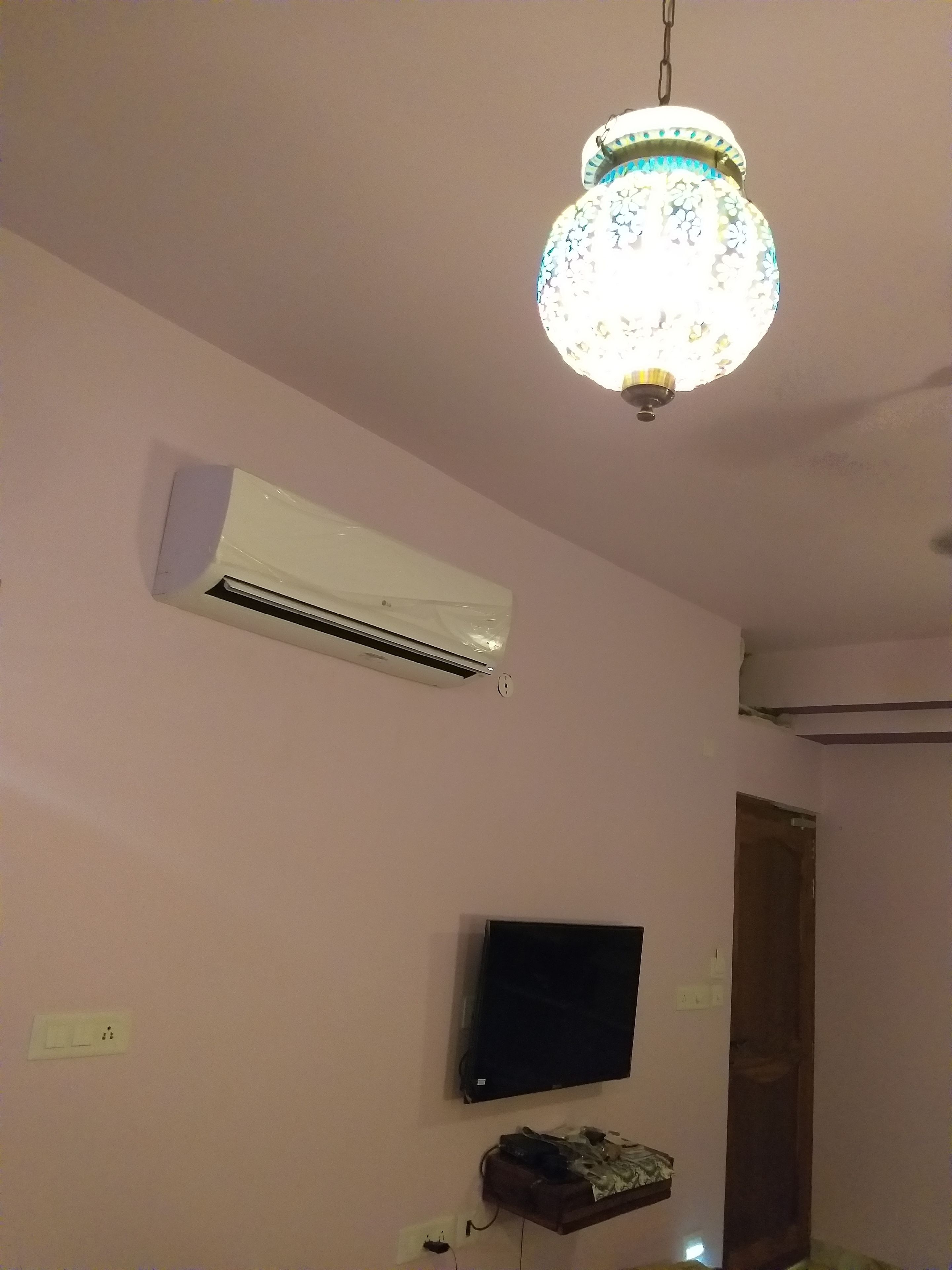 A room with a mounted air conditioner, a flat-screen TV, and a decorative chandelier.