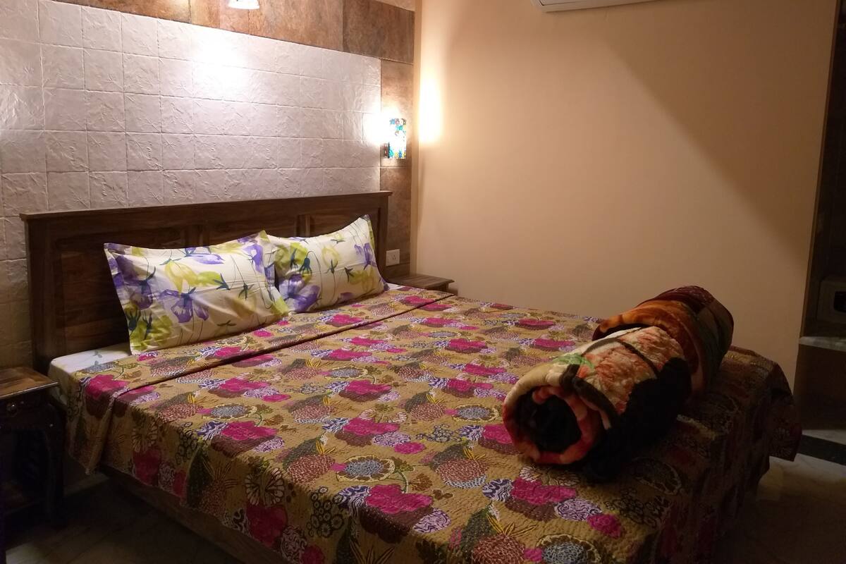 A bedroom with a wooden headboard, floral bedding, and an air conditioning unit above the bed.