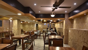 A restaurant with wooden tables and chairs, a ceiling fan, and patterned walls. - Prem Niwas Boutique Hotel (Jaipur)