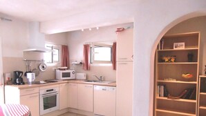 A compact kitchen with white cabinets, a microwave, a stove, and a sink. There is a small window with curtains, and a bookshelf with various items. - 2026 Comfort rental private heated pool 2 bedrooms air conditioning (Porto-Vecchio)