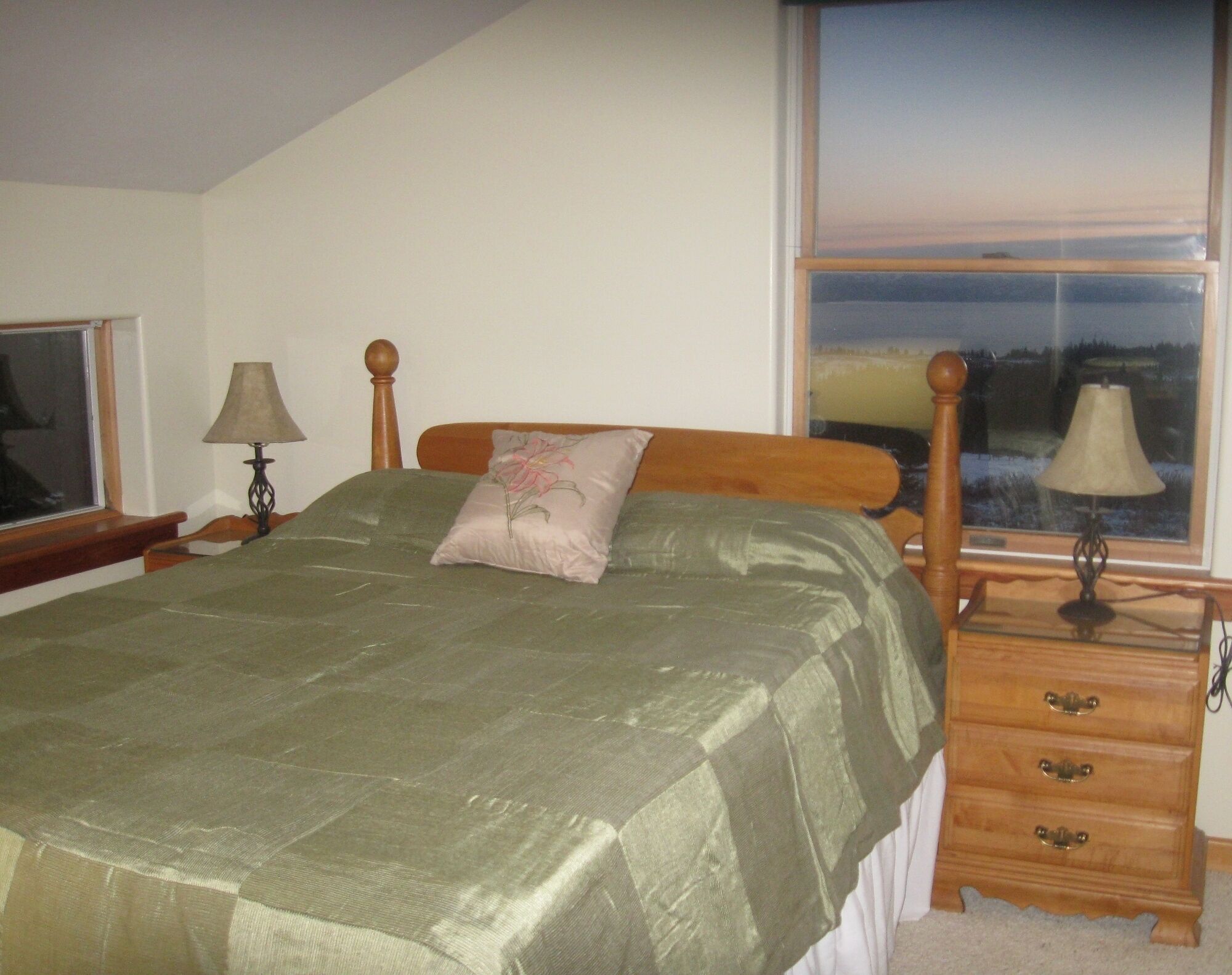 A bedroom with a bed, a nightstand, a lamp, a dresser, and a window with a view.