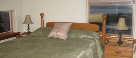 A bedroom with a bed, a nightstand, a lamp, a dresser, and a window with a view.