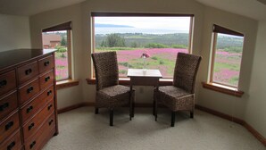 Ein Zimmer mit Blick auf ein Blumenfeld durch große Fenster, ein Holzkleiderschrank und zwei Korbstühle.