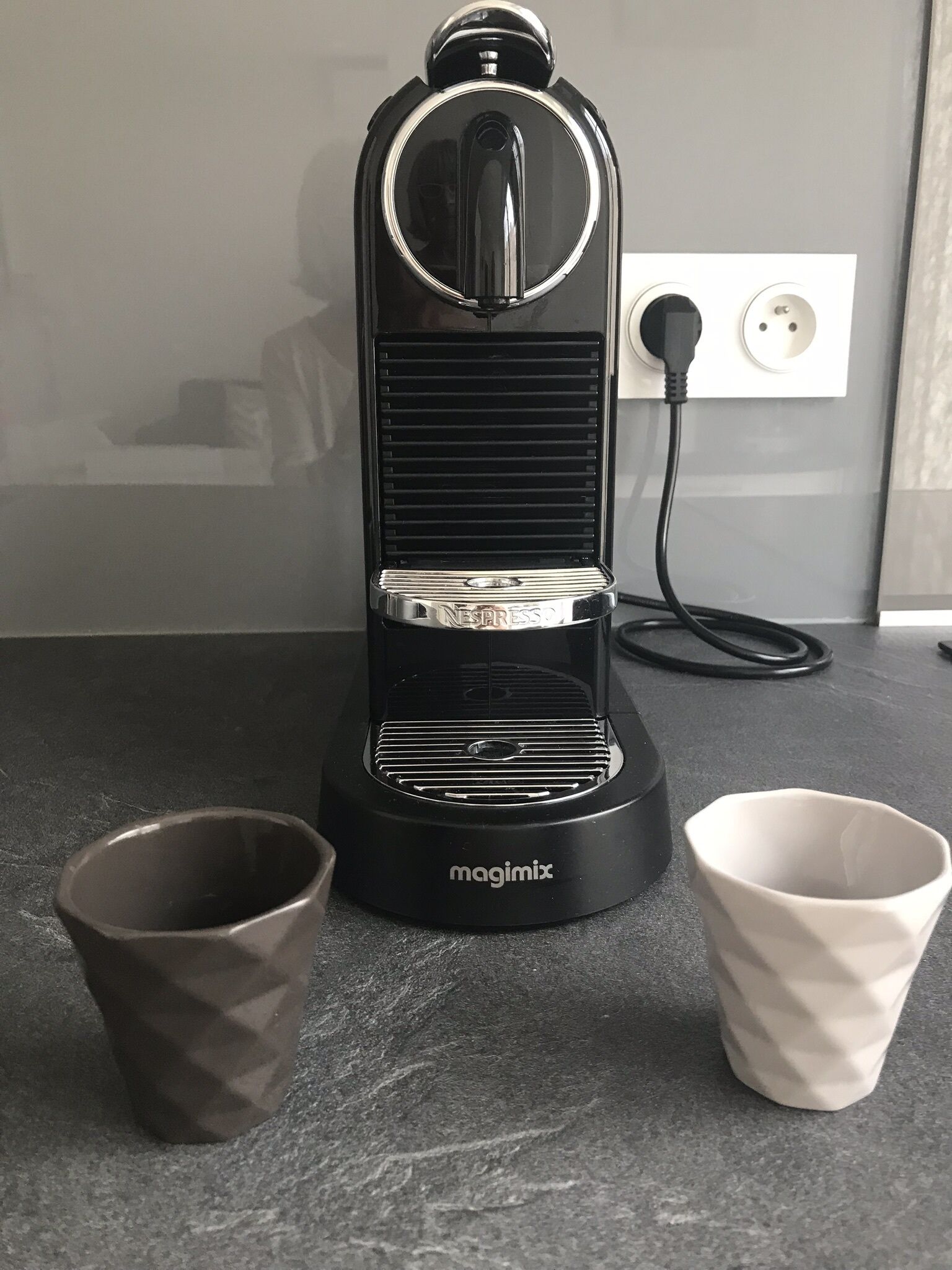 A kitchen with a coffee maker, two cups, and a power outlet.