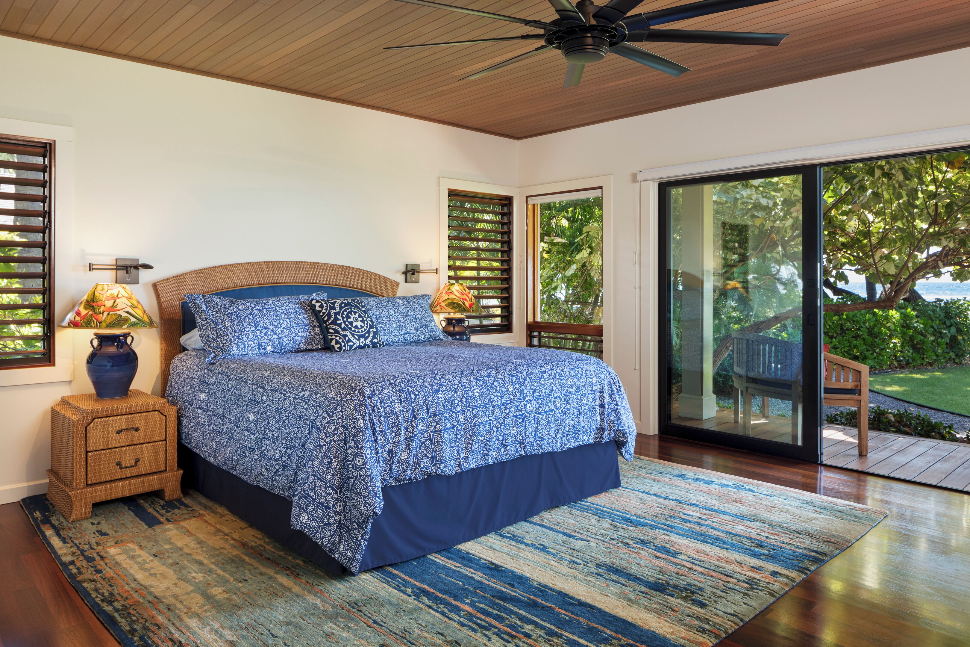 A bedroom with a large bed, a ceiling fan, and a view of the outdoors through a sliding glass door.