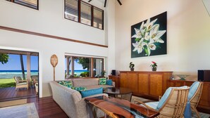 A spacious living area with a view of the ocean, a wooden coffee table, and a large painting of flowers on the wall.