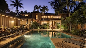 A resort with a swimming pool, palm trees, and a covered outdoor area.