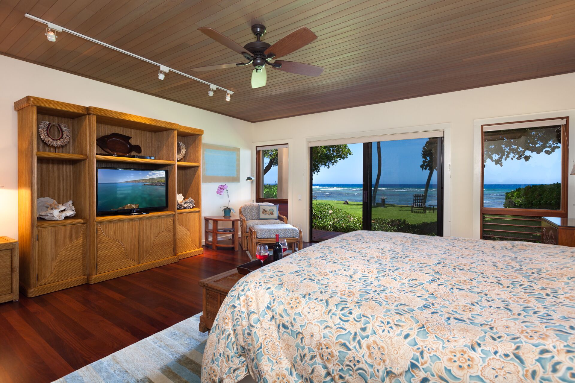 A bedroom with a large bed, wooden shelving, a television, and a view of the ocean through large sliding doors.
