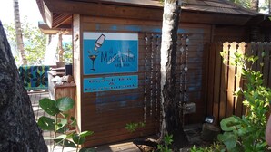 Un bar et un restaurant de plage en bois, appelé « El Mosquito Art Bar », avec une enseigne, entourés de palmiers et d’une clôture en bois.