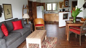 Een knusse woonkamer met een grijze bank, rode kussens, een houten salontafel en een vloerkleed met dessin.