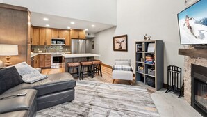 Ein modernes Wohnzimmer mit einer Couch, Kamin, Fernseher und Küchenbereich mit Holzschränken und einer Bar.