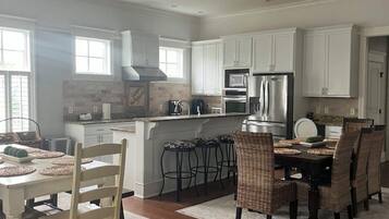 Una cocina amplia con armarios blancos, un comedor con mesa y sillas, y una isla grande con refrigerador y microondas.