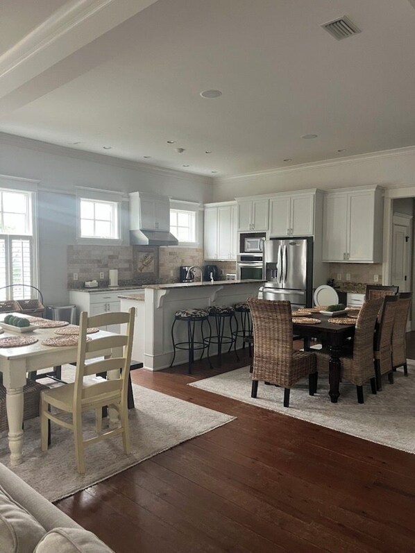 A spacious kitchen with white cabinets, a dining area with a table and chairs, and a large island with a refrigerator and microwave.