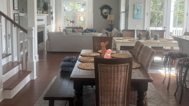 Een ruime woonkamer met een eethoek, met een groot raam, een open haard en een trap naar een ander niveau.