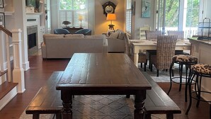 Een ruime woonkamer met een houten tafel, een bank en een eethoek met rieten stoelen.
