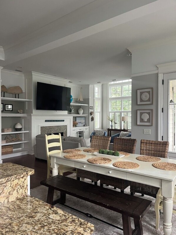 A dining area with a white table set for six, surrounded by wicker chairs.