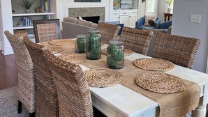 Een eetruimte met een witte tafel, rieten stoelen en decoratieve glazen potten.