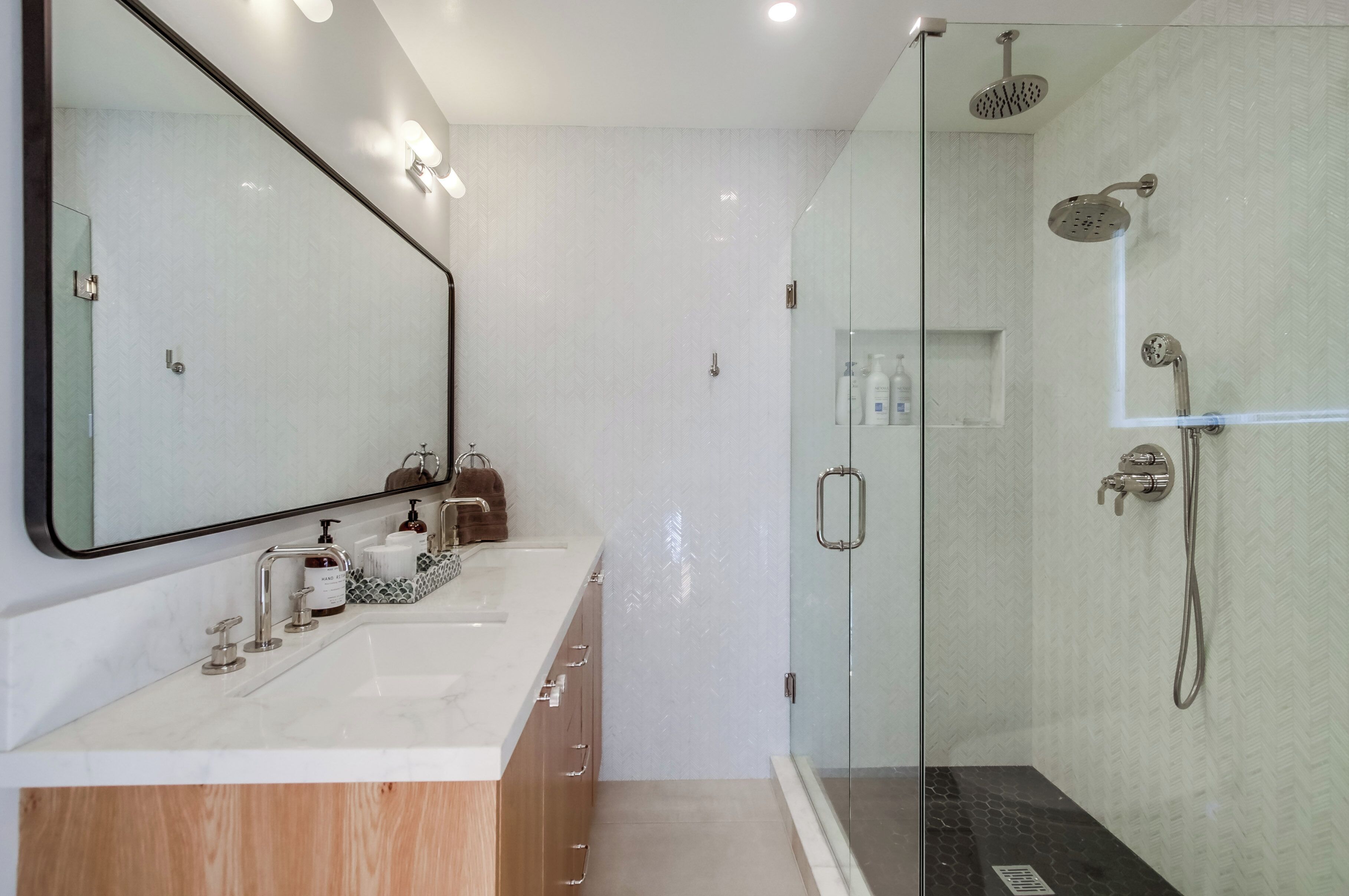 A modern bathroom with a glass-enclosed shower, a large mirror, and a vanity with a white countertop.