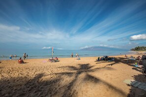 Een strand met mensen die zonnebaden en zwemmen, een bewakingspost en een heldere lucht.