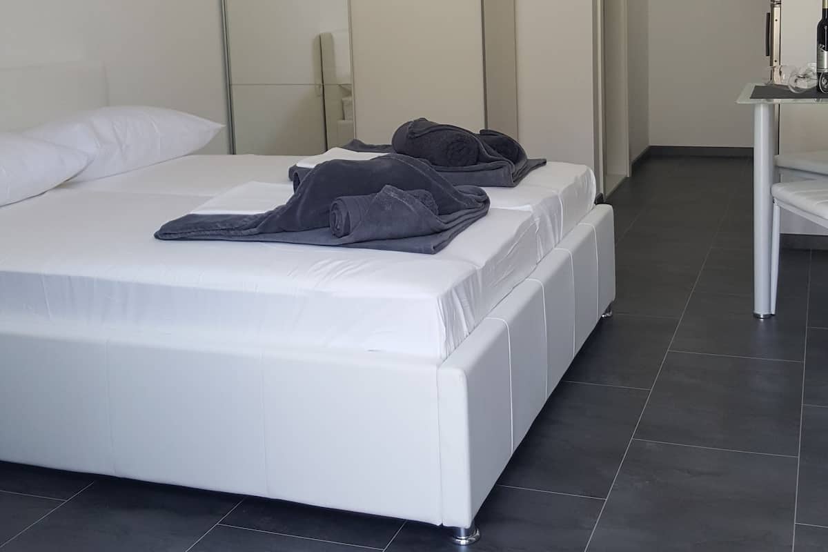 Un dormitorio moderno con una cama grande, una araña, un armario y una mesita con una botella.