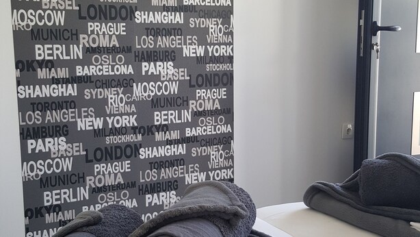 Quarto de hotel com cama, toalha dobrada e parede com nomes de cidades.