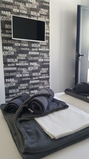 A hotel room with a bed, a folded towel, and a wall with city names. - Grey house (Makarska)