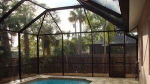 A swimming pool with a tiled deck, surrounded by a metal fence and trees. - Luxurious Naples Florida Villa! Close to Vanderbilt Beach! ☀️🌴🌅 🌴 (Naples)