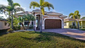 A two-story house with a brown garage, surrounded by a well-maintained lawn and palm trees. - Luxurious Naples Florida Villa! Close to Vanderbilt Beach! ☀️🌴🌅 🌴 (Naples)