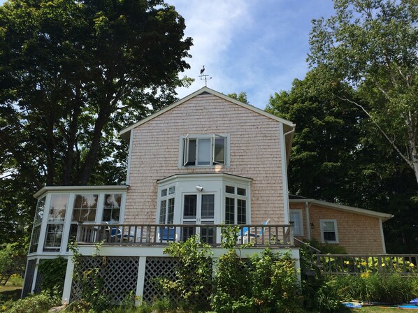A two-story house with a bay window, a covered porch, and a fenced yard. - Beautiful Seaside Home with Sweeping Views - Weekly Discounts Available! (Mt Desert)