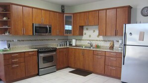 A kitchen with wooden cabinets, stainless steel appliances, and a tiled floor. - Spacious, attractively decorated 2 BR 1bath gated Apt, 4 Mins to Jobos Beach (Isabela)
