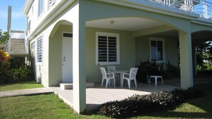 A two-story house with a covered patio, white outdoor furniture, and a small garden area. - Spacious, attractively decorated 2 BR 1bath gated Apt, 4 Mins to Jobos Beach (Isabela)