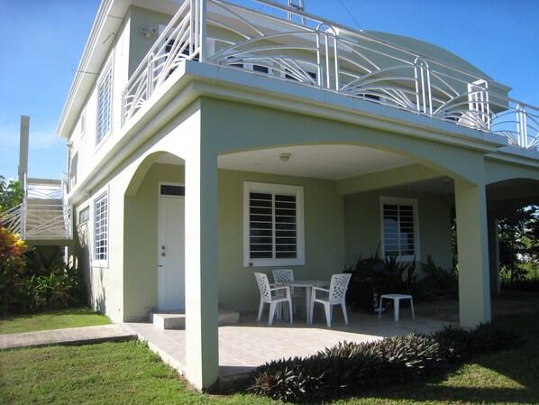 A two-story house with a covered patio, white outdoor furniture, and a small garden area.