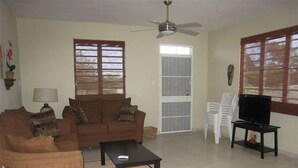 A living room with a sofa, coffee table, TV, and windows with blinds. - Spacious, attractively decorated 2 BR 1bath gated Apt, 4 Mins to Jobos Beach (Isabela)