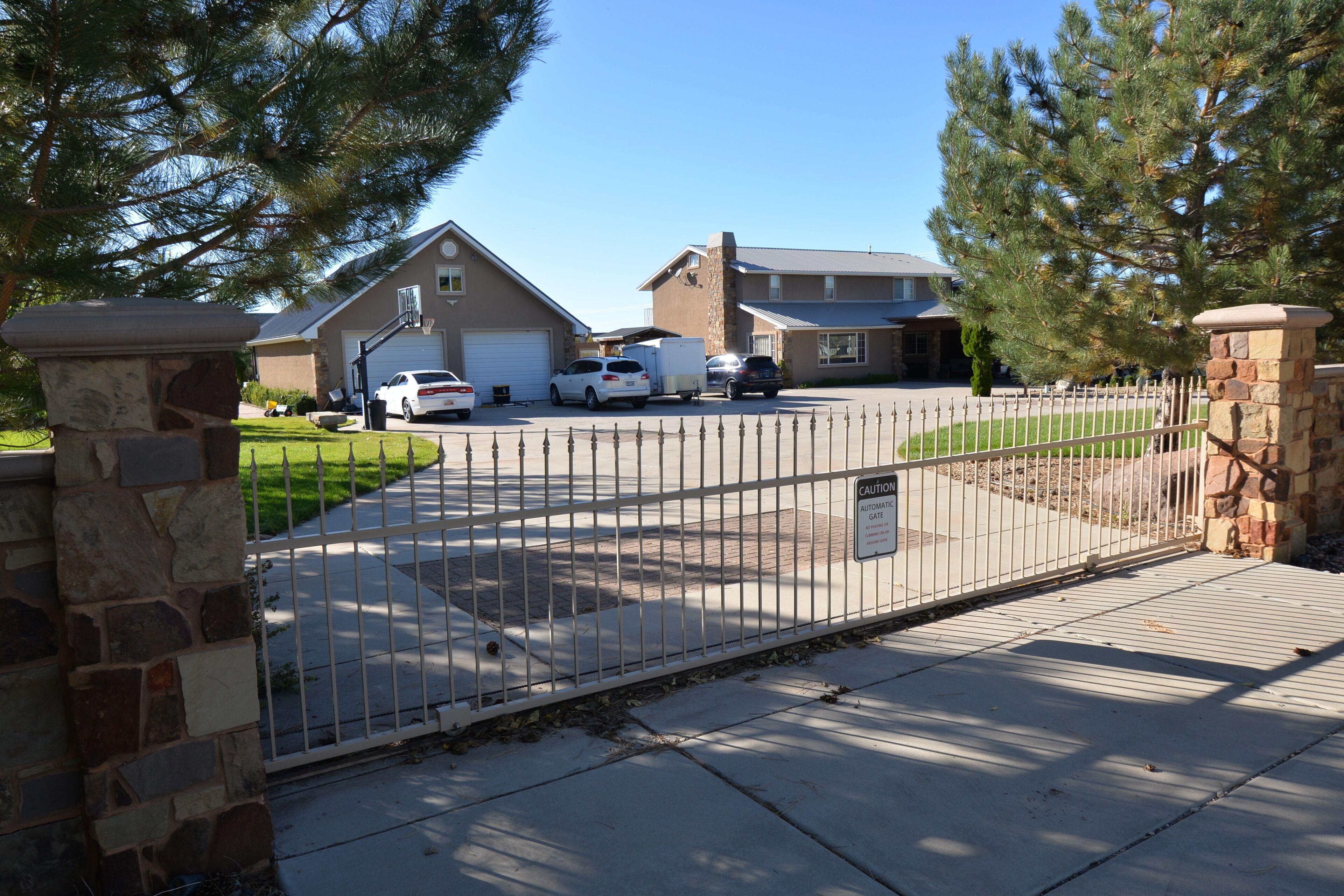 A gated driveway leading to a house with a garage, a stone wall, and a metal gate.