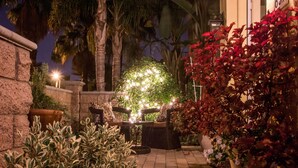 A well-lit outdoor patio area with a seating arrangement, potted plants, and a decorative light display. - Come stay at our spacious beach house! (Oceanside)