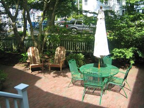 A patio with a round table and chairs, a wooden fence, and a street with parked cars in the background. - Historic Sea Captains Home in Nantucket! Perfect for Large Groups and Families (Nantucket)