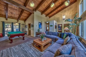 A spacious living room with a pool table, a large sofa, and a wooden ceiling.
