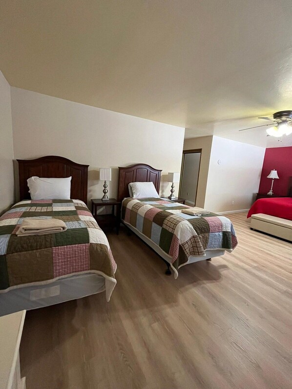 A hotel room with two beds, wooden flooring, and a red accent wall.