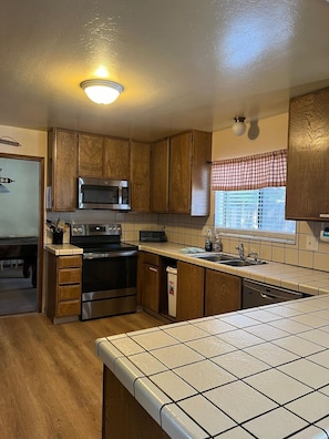 A compact kitchen with wooden cabinets, a microwave, an oven, and a dishwasher. - Meadow Drive Home In Beautiful Lake Tahoe Nevada (Stateline)