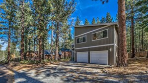 A two-story building with a garage, surrounded by tall pine trees. - Meadow Drive Home In Beautiful Lake Tahoe Nevada (Stateline)