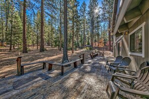 A wooden deck with benches and chairs, surrounded by tall pine trees. - Meadow Drive Home In Beautiful Lake Tahoe Nevada (Stateline)